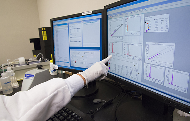 A hand points at medical data and information displayed on two computer screens